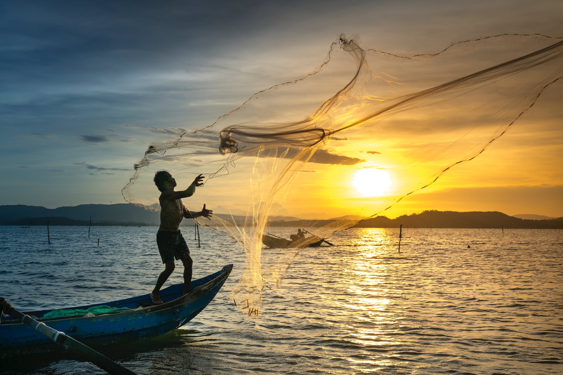 person throwing fish net while standing on boat